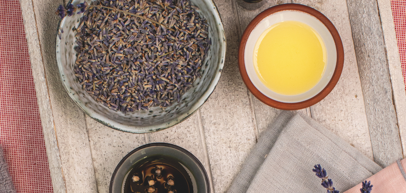 Schale mit getrockneten Lavendelblüten und Schalen mit Öl auf rustikalem Tisch arrangiert.
