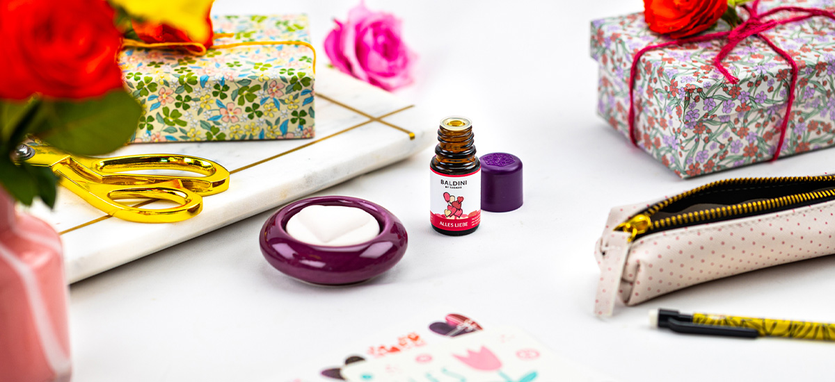 Baldini „Alles Liebe“ Duftkomposition zwischen Geschenkverpackungen, Rosen, Schere und weiteren Bastelutensilien dekorativ arrangiert.