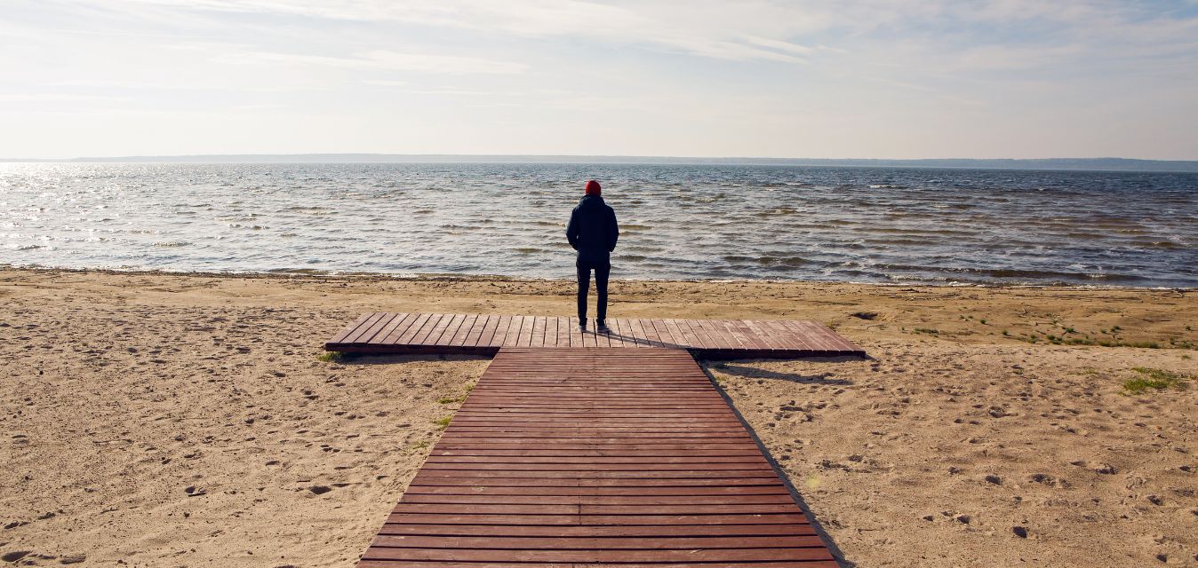 Mensch, der am Strand steht und aufs Meer blickt.