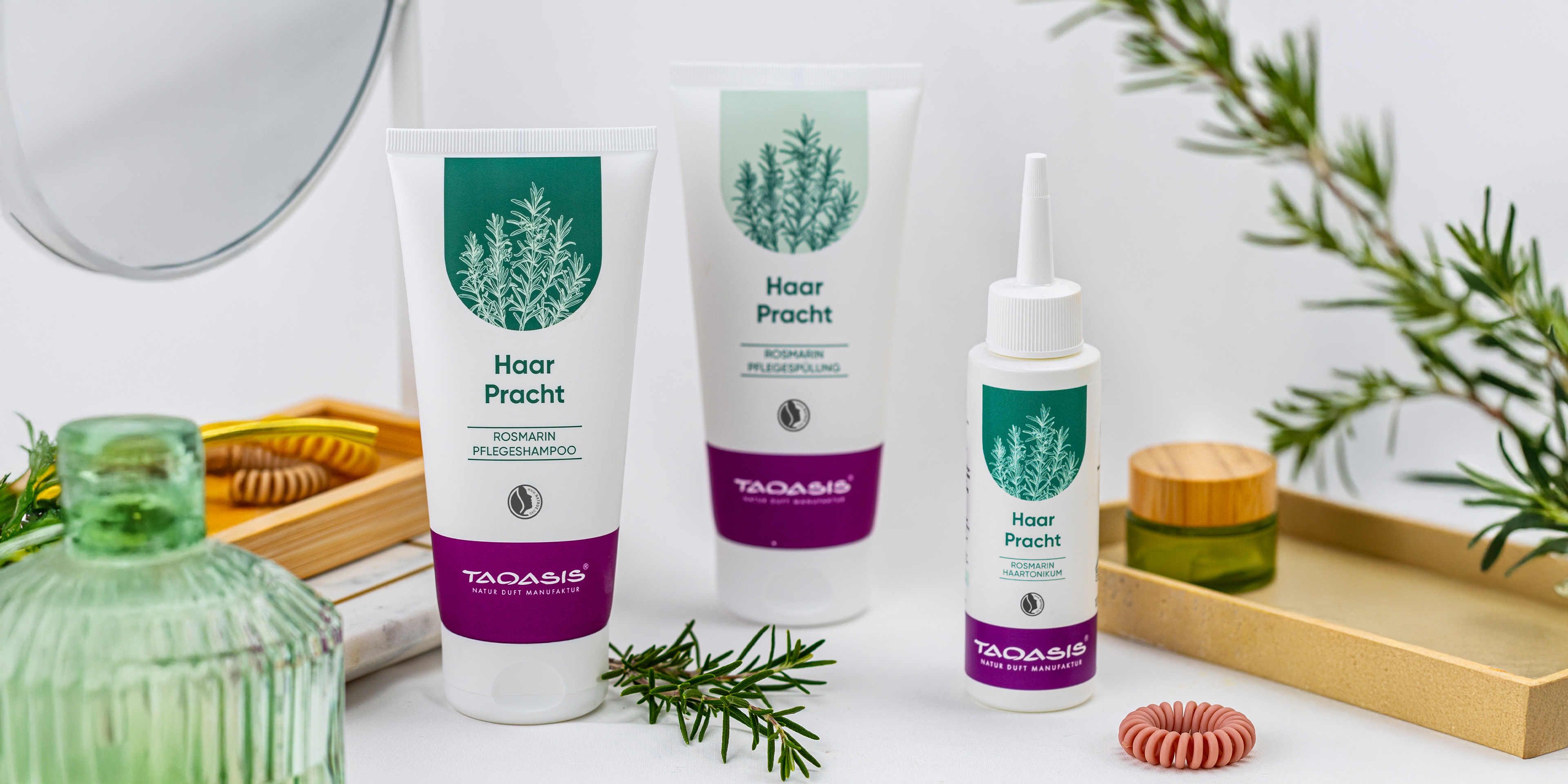 Rosmarin-Haarpflege mit Pflegeshampoo, Pflegespülung und Haartonikum, dekoriert mit frischen Rosmarinzweigen und Pflegeaccessoires.