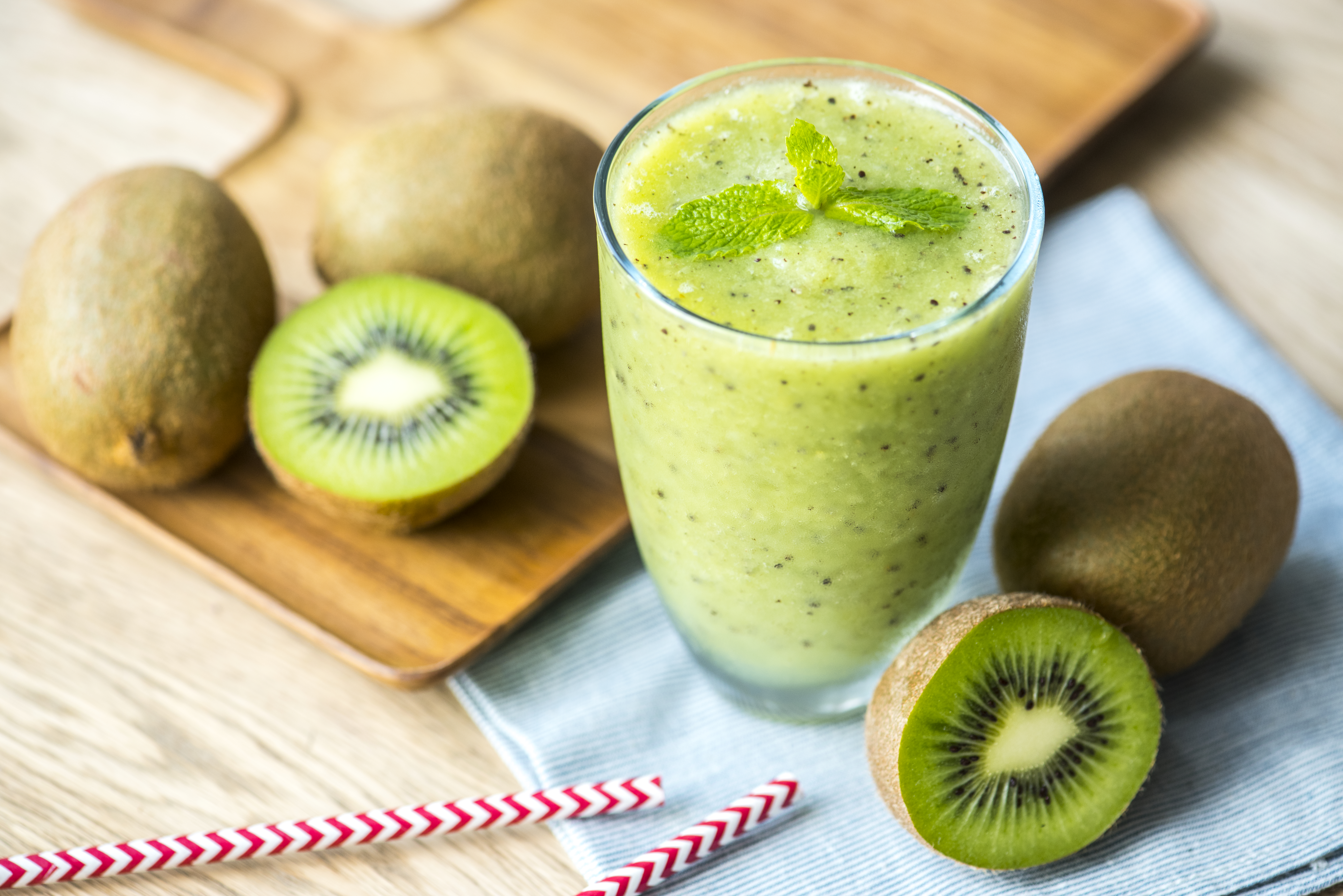Grüner Kiwi-Smoothie im Glas mit frischer Minze, umgeben von Kiwis.