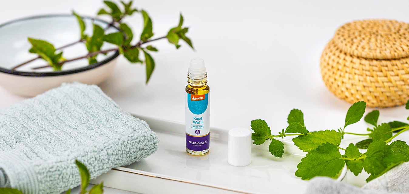 TAOASIS Kopfwohl Roll-On neben frischer Minze, Handtüchern und natürlichen Badeaccessoires in heller Umgebung.
