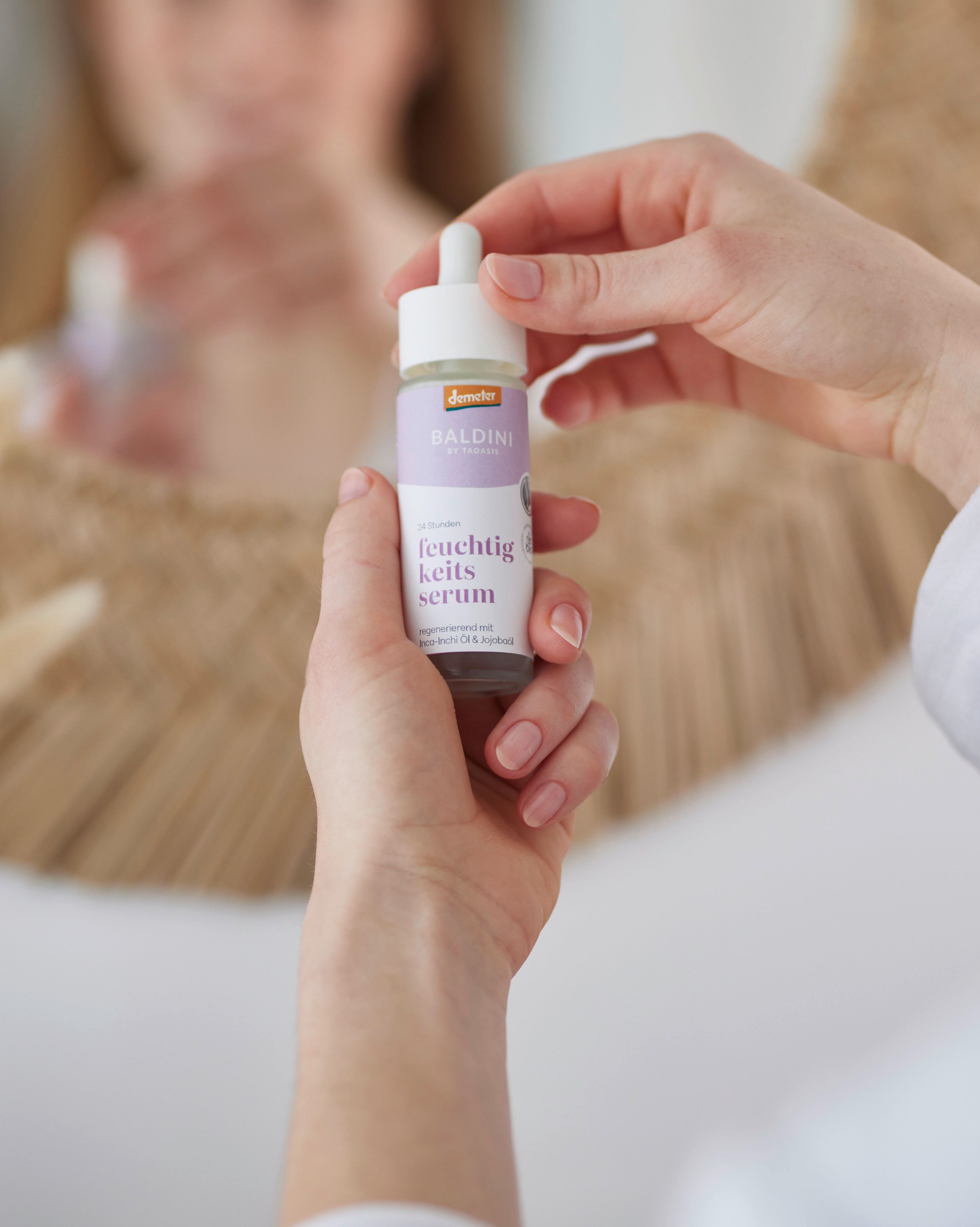 Baldini Feuchtigkeitsserum wird in der Hand gehalten von einer Frau, die sich im Spiegel spiegelt. 