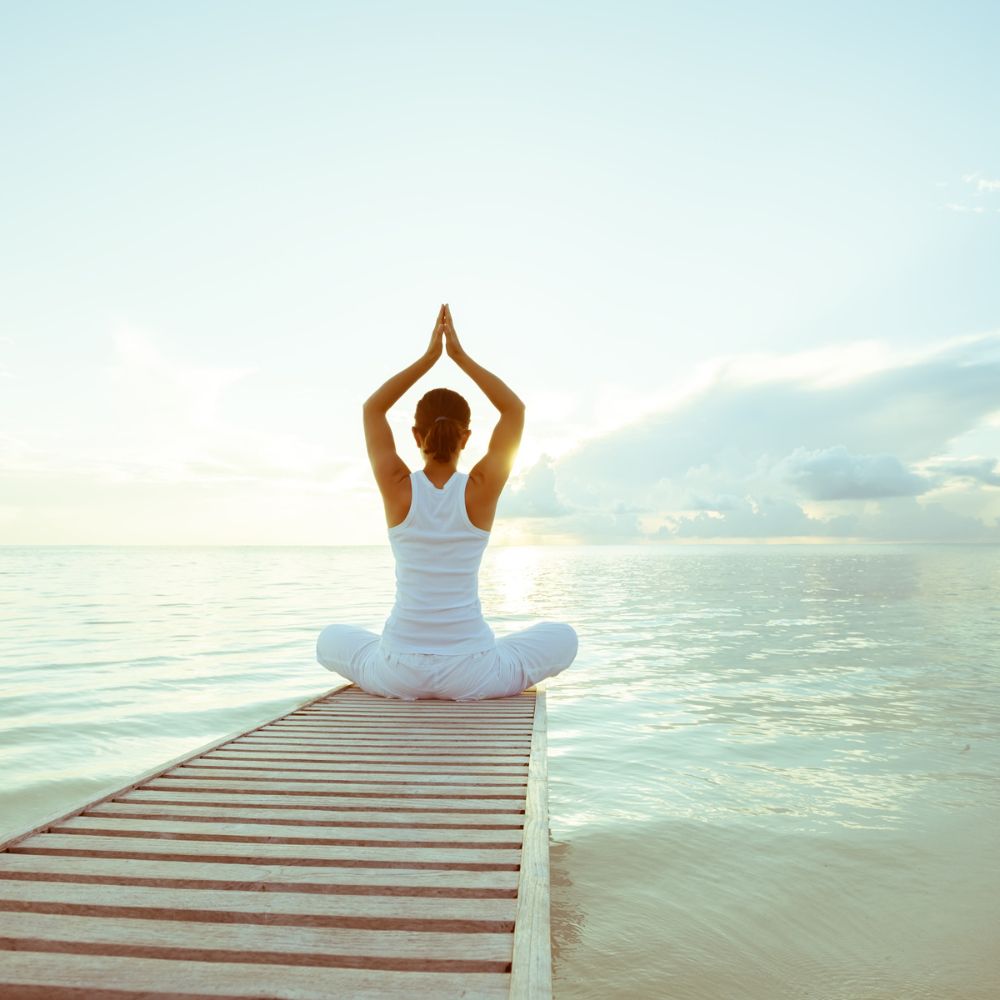 Frau sitzt auf Steg über dem Wasser und macht Yogaübung