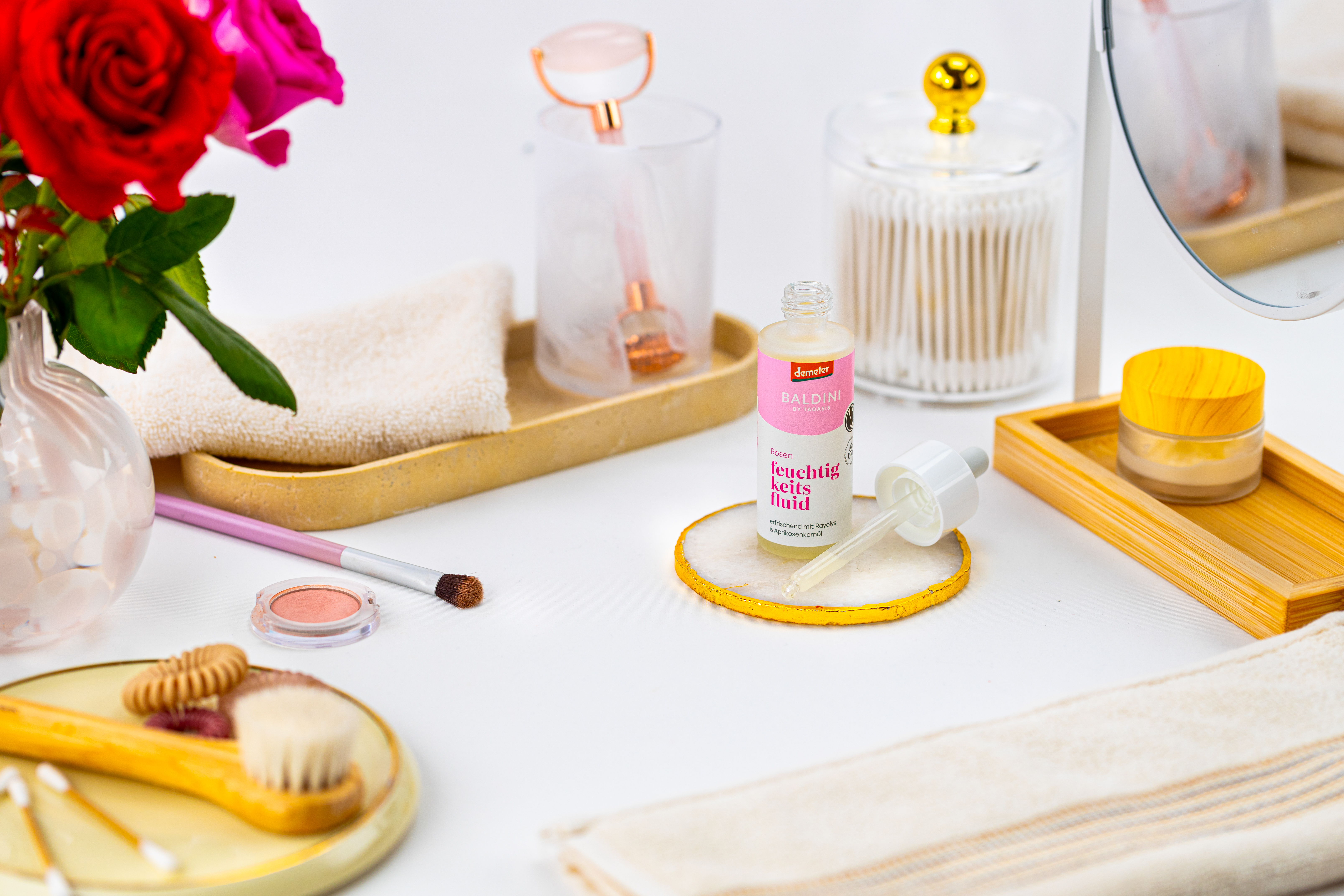 Baldini Rosen Feuchtigkeitsfluid mit Pipette, umgeben von Rosen und Beauty-Accessoires.
