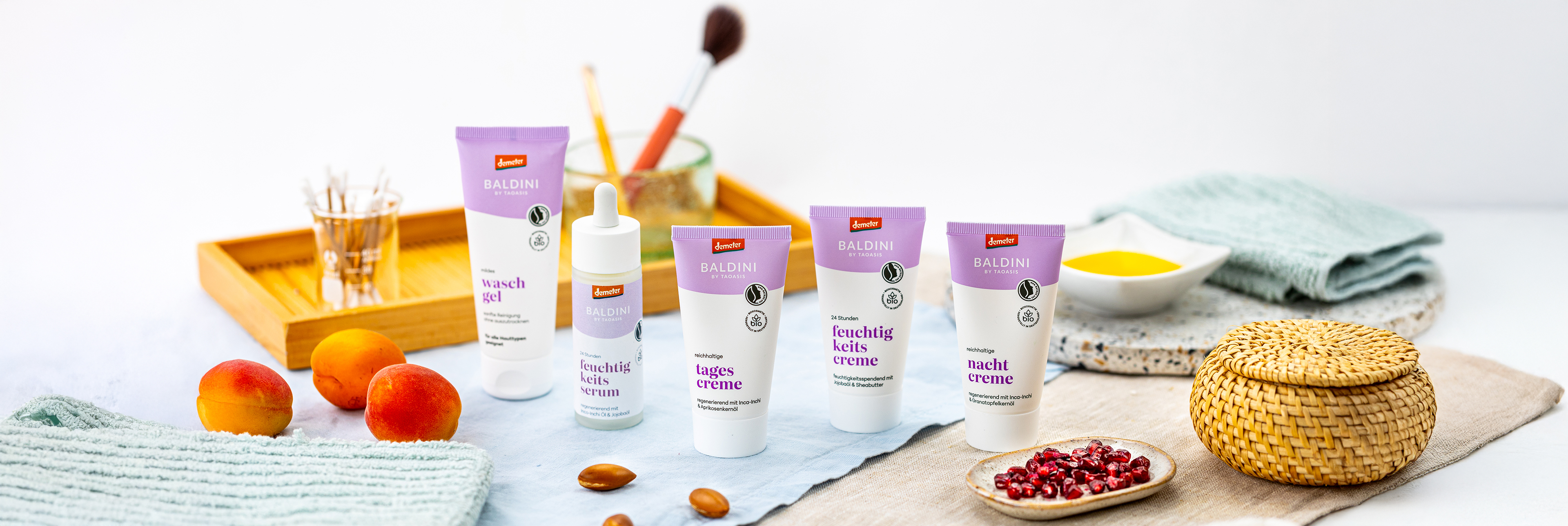 Lavendelserie mit Deko wie Ost, Handtüchern und einer Tischdecke. Im Hintergrund sind Kosmetikutensilien.