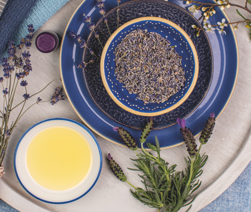 Schale mit getrockneten Lavendelblüten, umgeben von frischem Lavendel und einer Schale mit Öl.