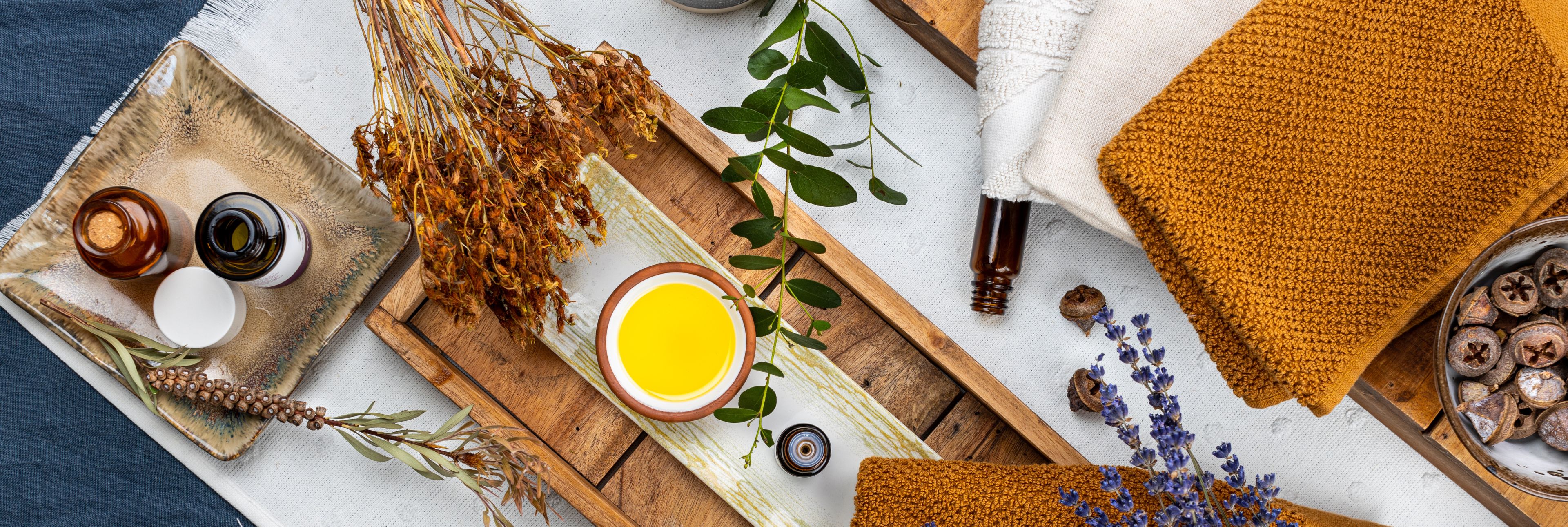 Das Bild zeigt eine warme, naturverbundene Szene mit Massageölen, getrockneten Kräutern und Handtüchern in Erdtönen – es vermittelt Kraft, Geborgenheit und wohltuende Entspannung.