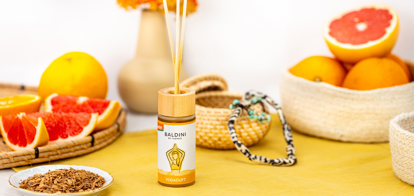 Baldini Yogaduft Raumduft mit Duftstäbchen, dekoriert mit Grapefruits, Orangen und natürlichen Accessoires in warmen Gelbtönen.