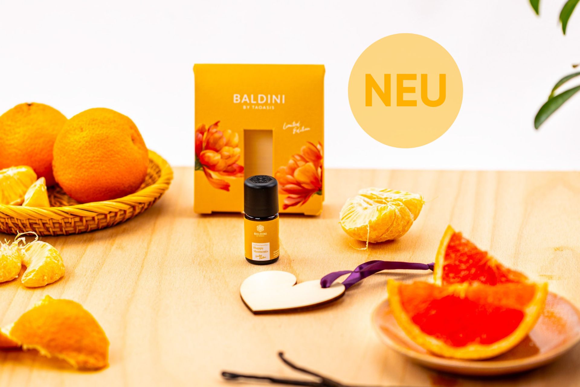 Baldini Happy Moments Duftset mit ätherischem Öl und Duftanhänger, umgeben von Orangen und Grapefruit auf einem Holztisch.