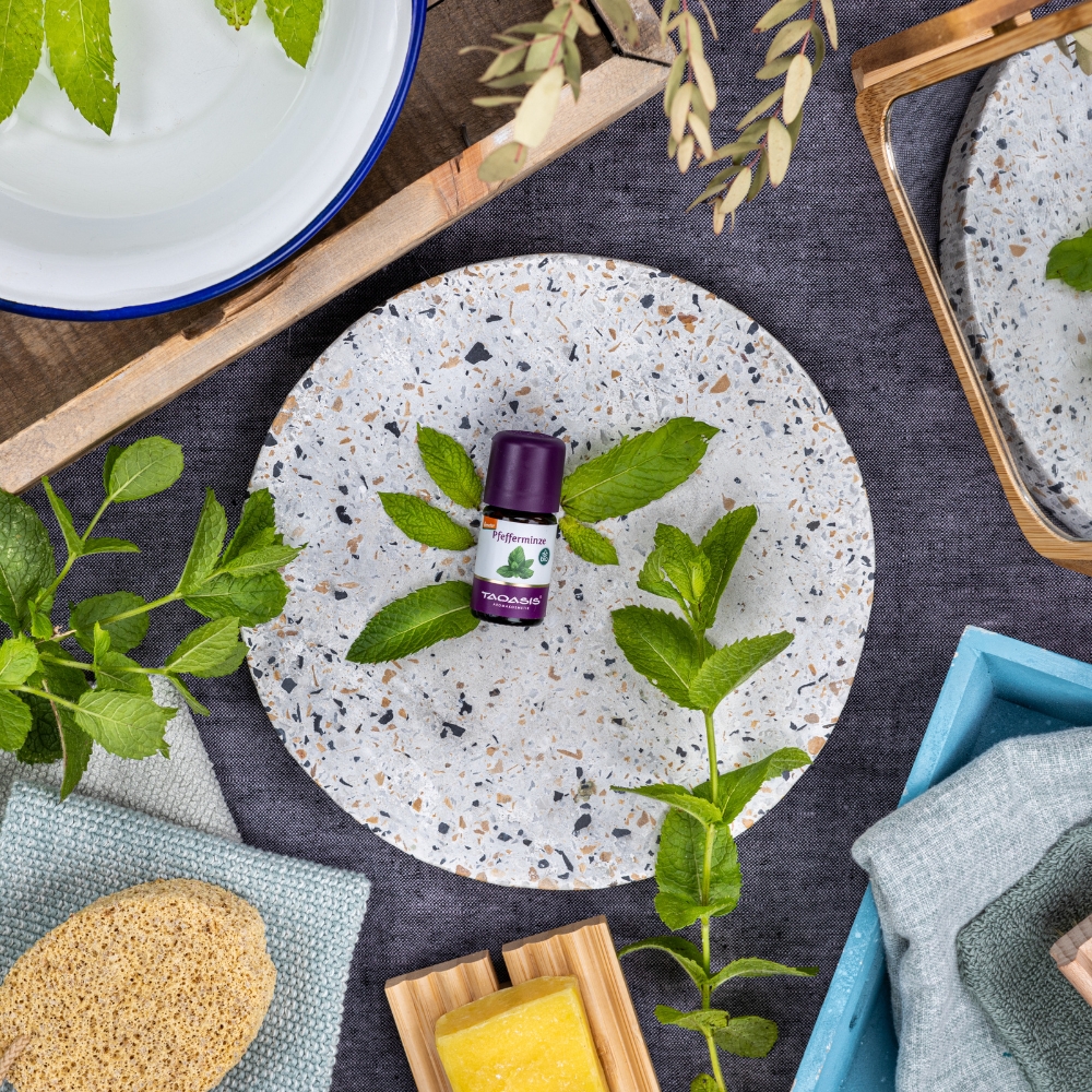 Ätherisches Pfefferminzöl von TAOASIS auf einem Teller mit frischen Minzblättern.
