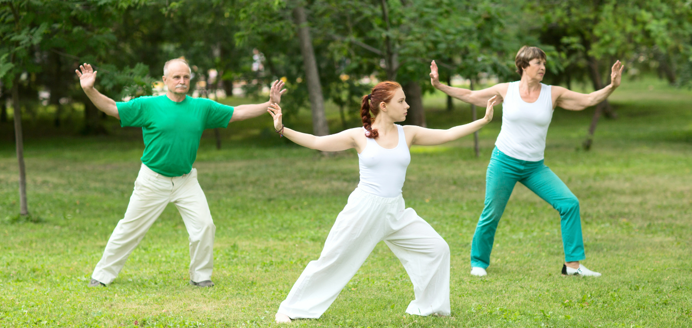 Ein Opa, eine Oma und eine junge rau machen Yoga im Park.