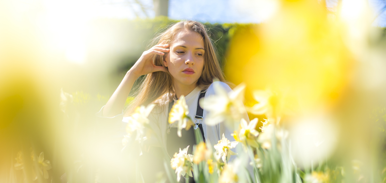 Frau sitzt nachdenklich zwischen Blumen.