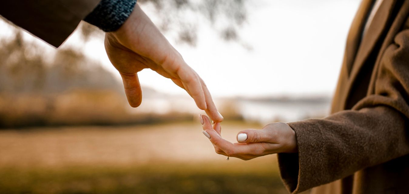 Zwei Menshcen, die sich die Hand reichen, im Hintergrund ist grüne Landschaft.
