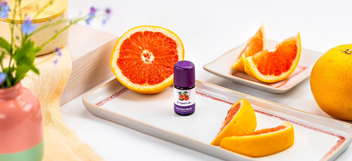 TAOASIS Grapefruitöl dekorativ mit frischen Grapefruitscheiben auf hellem Hintergrund arrangiert.