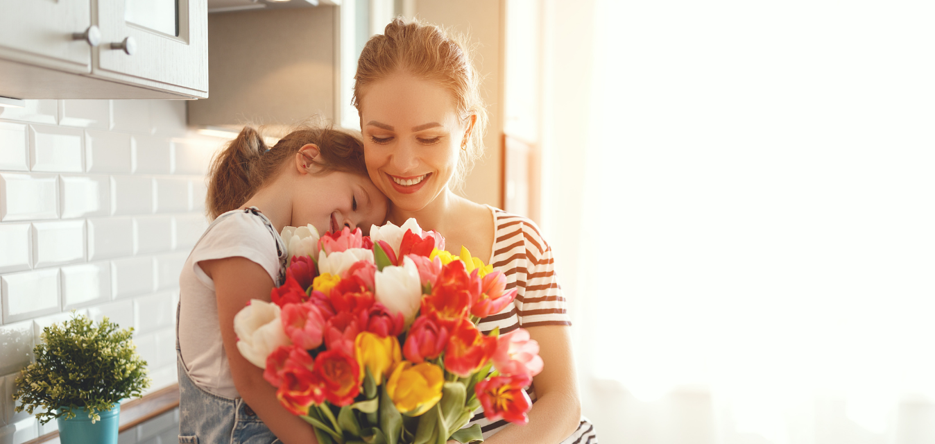 Mutter und Tochter sitzen schmusend in der Küche. Mutter hält einen Tulpenstrauch