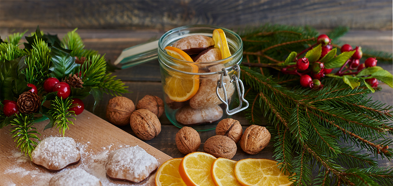 Weihnachtliches Arrangement mit Lebkuchen, Walnüssen, Orangenscheiben, Tannenzweigen und roten Beeren auf einem rustikalen Holztisch.