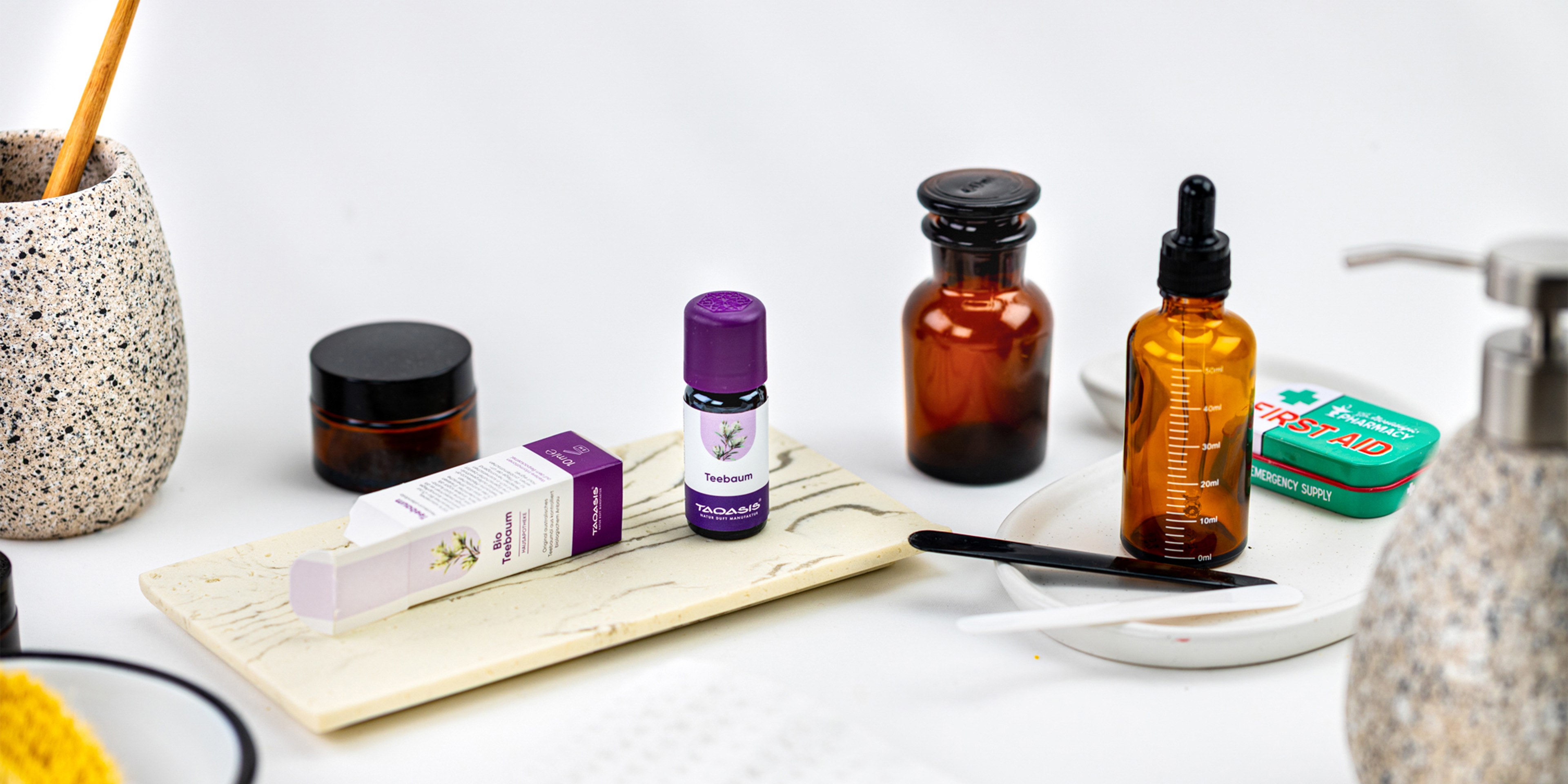 TAOASIS Teebaumöl mit Verpackung auf einer Ablage, umgeben von braunen Apothekerflaschen, Pipette und Erste-Hilfe-Accessoires.