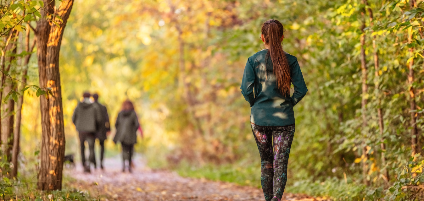 Frau joggt auf einem herbstlichen Waldweg zwischen bunten Bäumen.