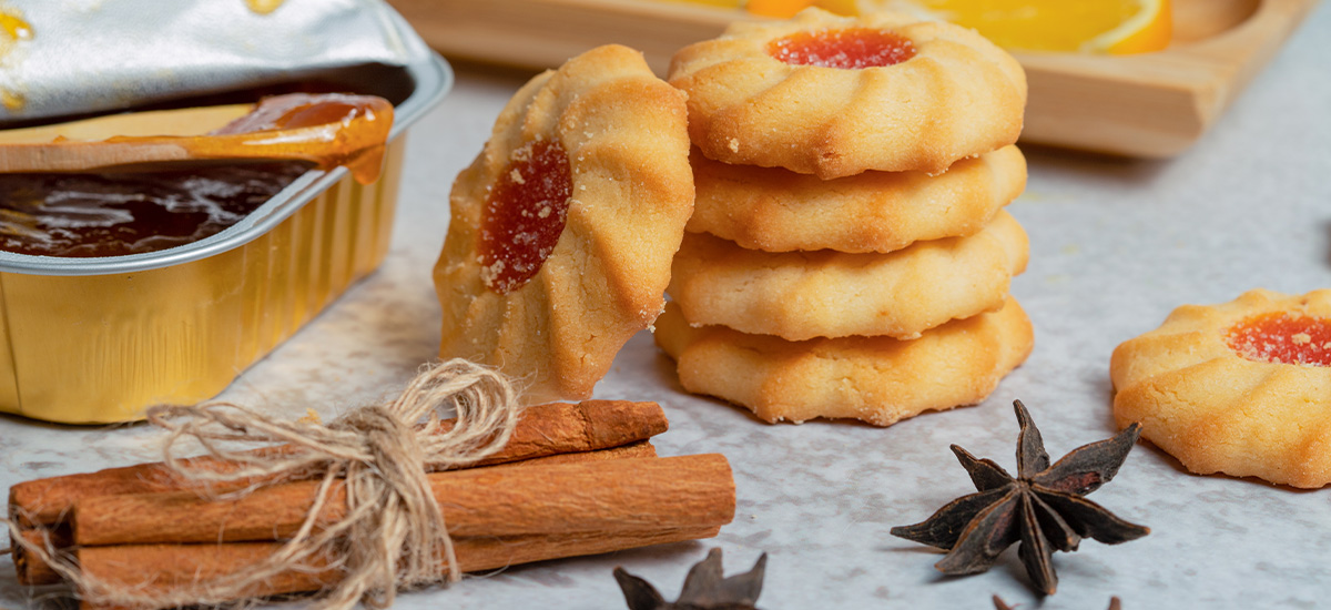 Winterliche Kekse mit fruchtiger Füllung, dekoriert mit Zimtstangen, Sternanis und Marmelade.