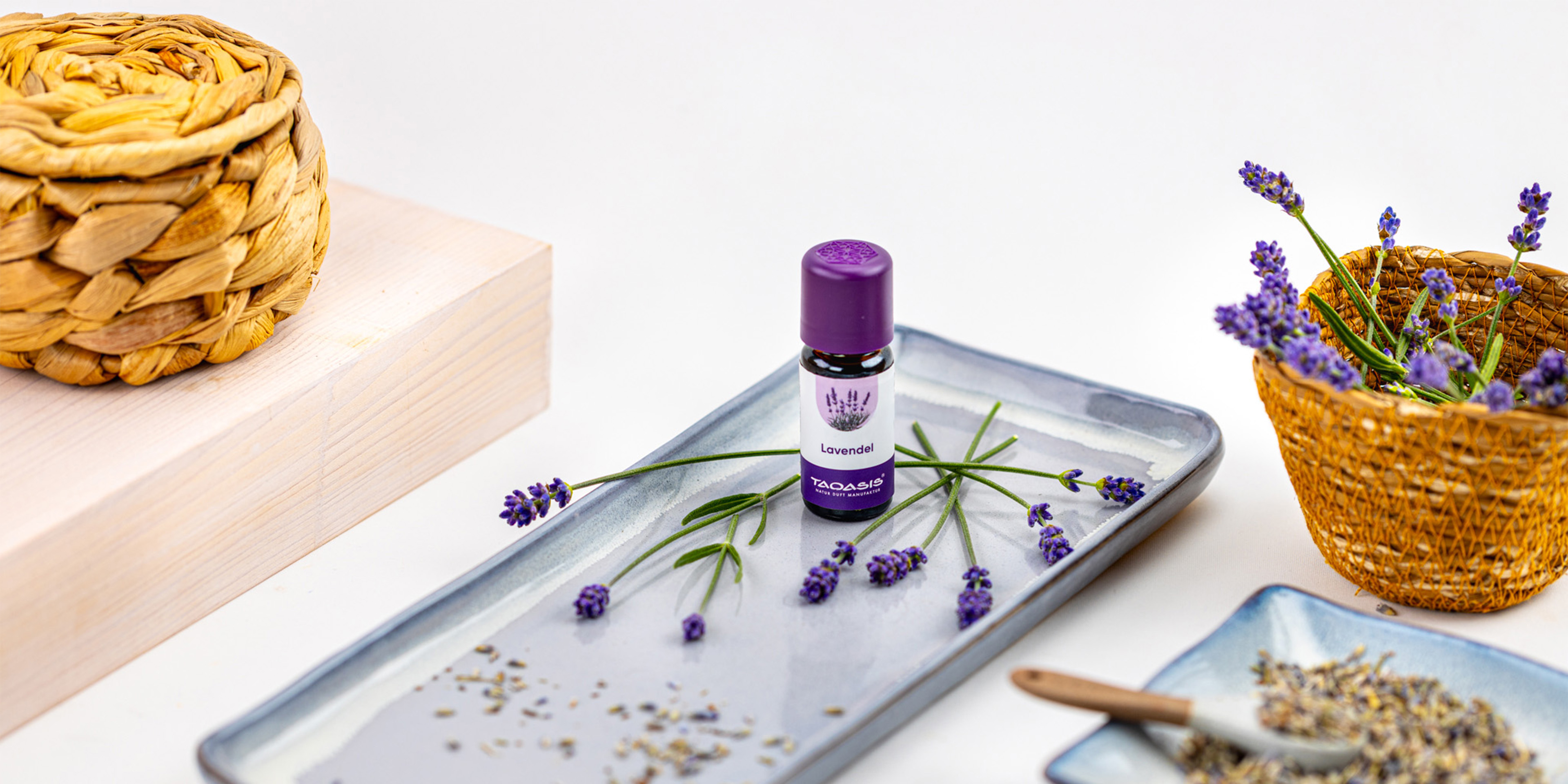 Fläschchen mit ätherischem Lavendelöl auf einer Keramikschale, dekoriert mit frischen Lavendelzweigen, getrockneten Blüten und natürlichen Körben.