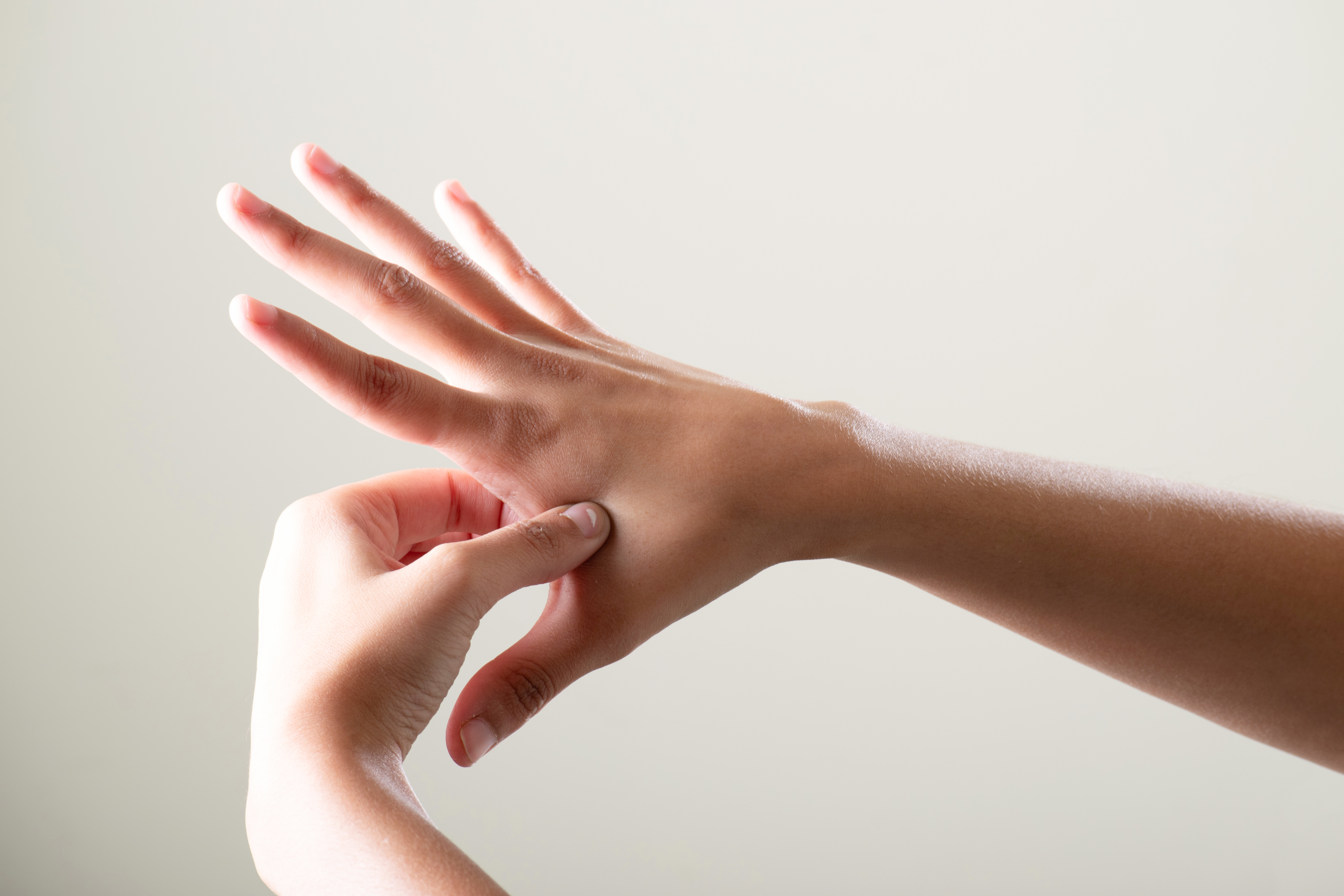 Person drückt einen Akupressurpunkt auf dem Handrücken mit dem Daumen.