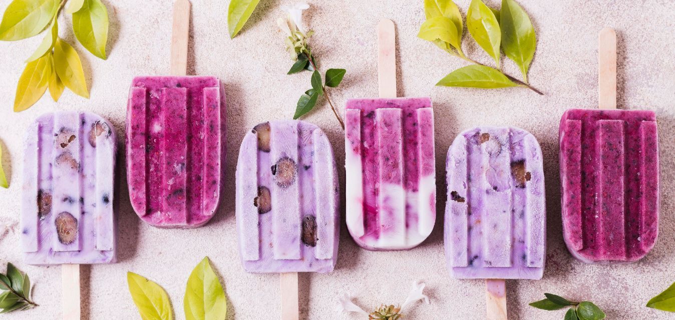 Selbstgemachte Eis am Stiel aus Beeren und Joghurt, dekoriert mit grünen Blättern.