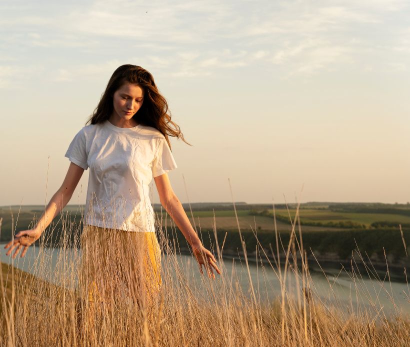 Frau, die durch hohes Gras geht. Im Hintergrund ist weite Landschaft und ein Fluss.