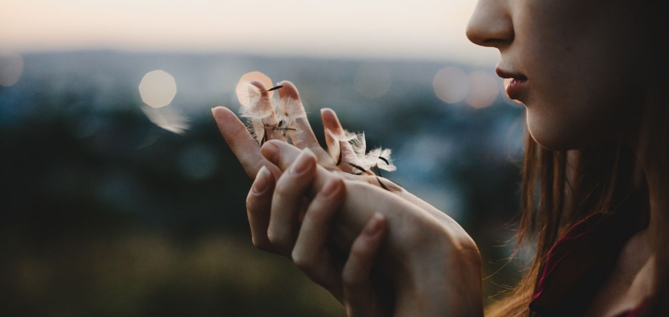 Frau hält Pusteblumensamen in der Hand.