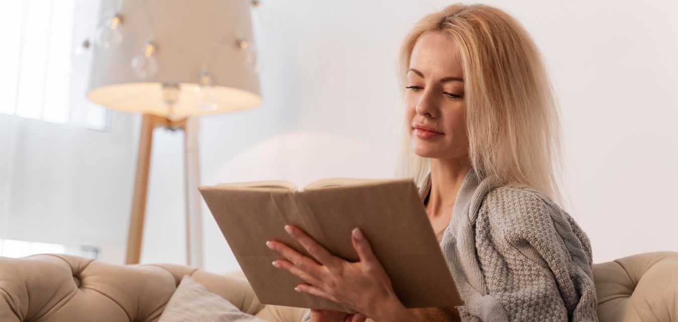 Frau liest entspannt ein Buch auf dem Sofa.
