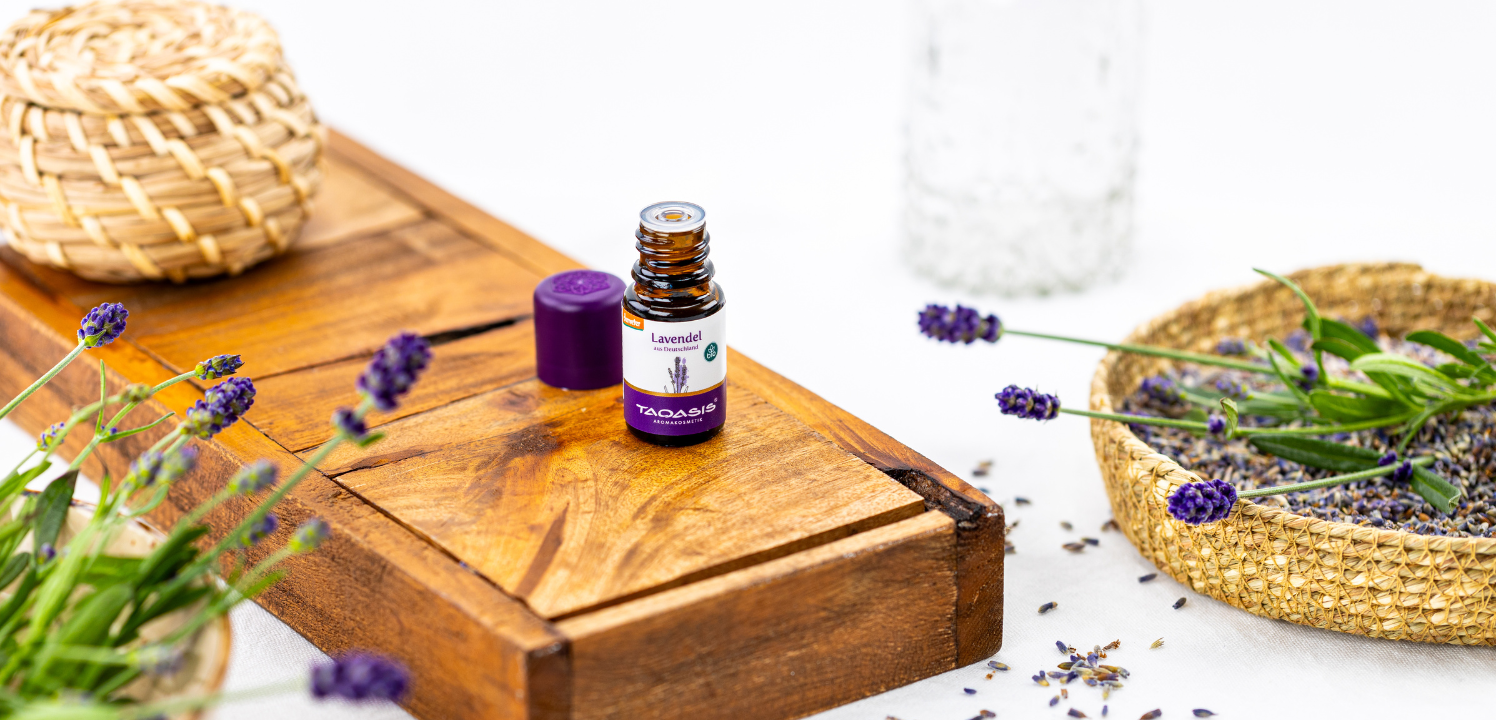 Ätherisches Lavendelöl von TAOASIS auf Holztablett mit Lavendelblüten