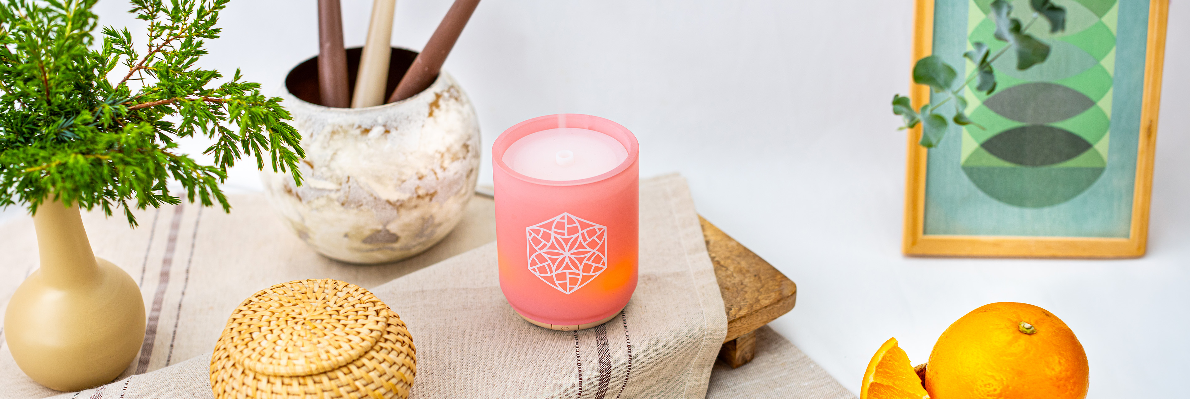 Duftgerät mit warmem Licht auf dekoriertem Tisch, umgeben von Pflanzen und natürlichen Materialien in wohnlicher Atmosphäre