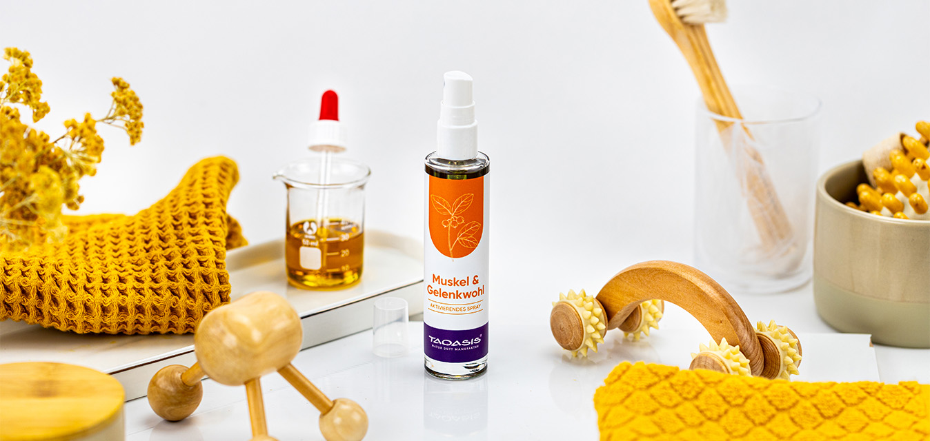 TAOASIS Muskel & Gelenkwohl Spray, umgeben von Massagehilfen, Pflanzenöl und gelben Pflegeaccessoires.
