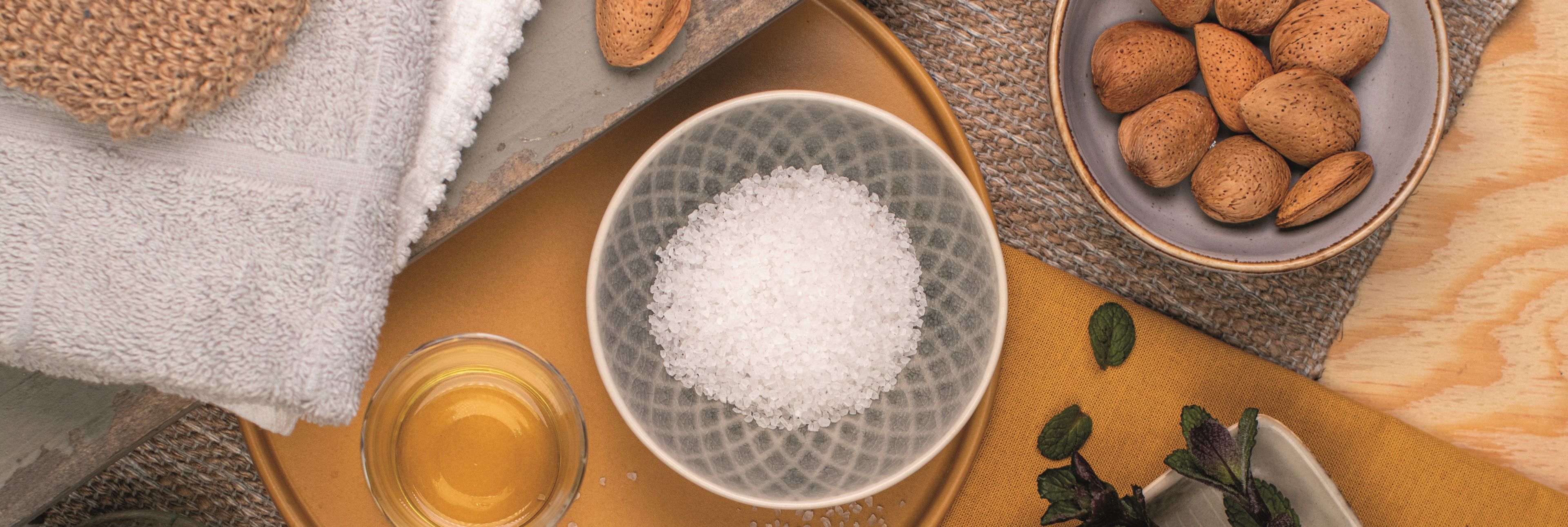 Das Bild zeigt eine ruhige Spa-Szene mit Meersalz, Mandeln, Öl und Handtüchern – in warmen Naturtönen arrangiert und perfekt für einen Moment der Entspannung und natürlichen Pflege.