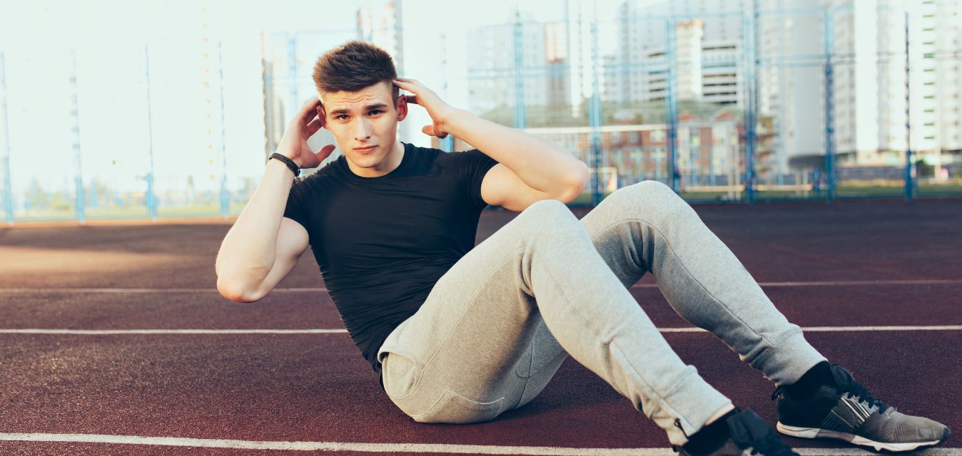 Mann auf Sportplatz sitzend und Sportübungen machend.