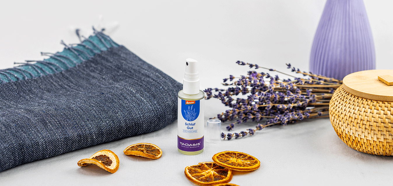 TAOASIS Schlaf-gut-Kopfkissenspray, umgeben von Lavendel, getrockneten Orangenscheiben, einer Decke und wohnlichen Accessoires.