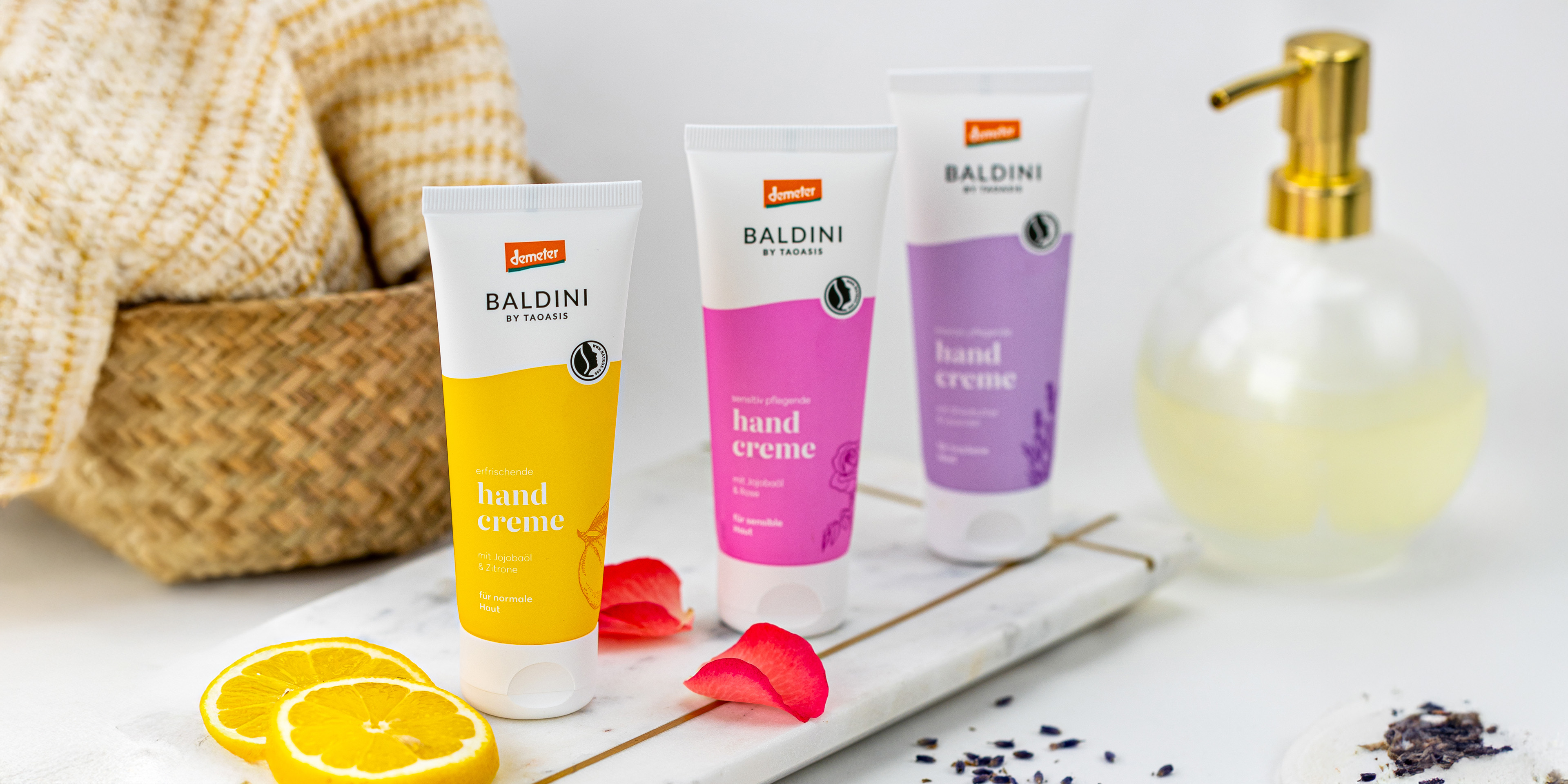 Baldini Handcremes Zitrone, Rose und Lavendel auf einer hellen Ablage, dekoriert mit Zitronenscheiben, Rosenblüten und Lavendel.