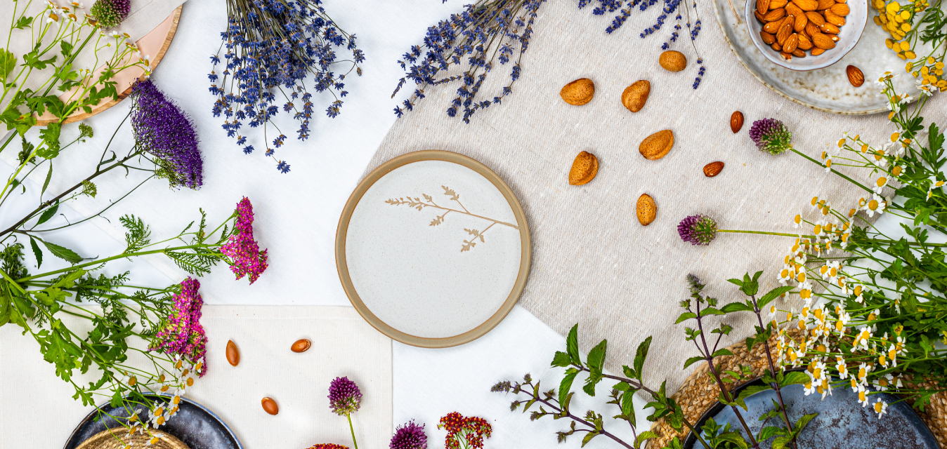 Natürliche Zutaten wie Kräuter, Blüten und Mandeln auf einem Tisch arrangiert