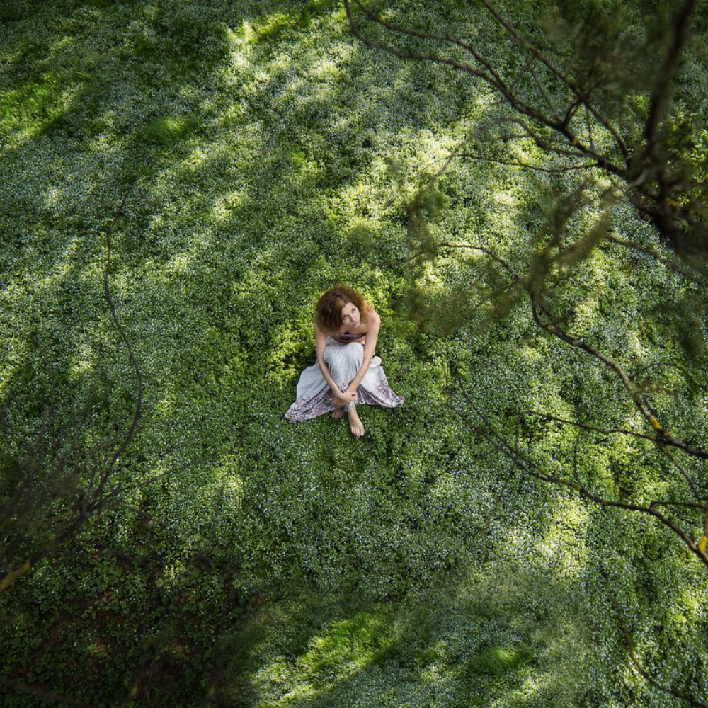 Frau die im Wald auf dem Boden sitzt, von oben fotografiert.