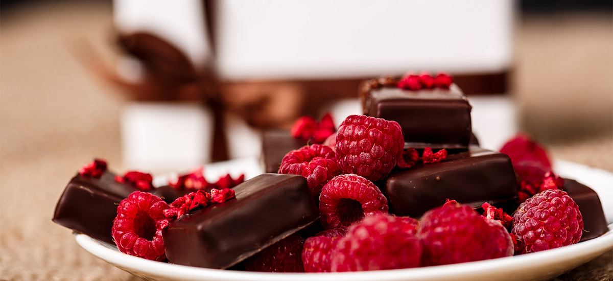 Schokoladenpralinen mit frischen Himbeeren und gefriergetrockneten Himbeerstückchen auf einem weißen Teller