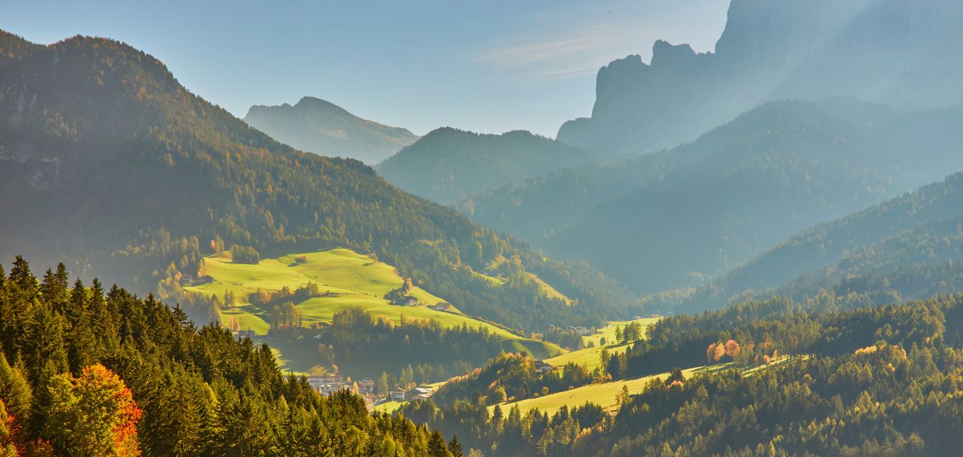 Sonnige Berglandschaft mit grünen Wiesen und Wäldern.