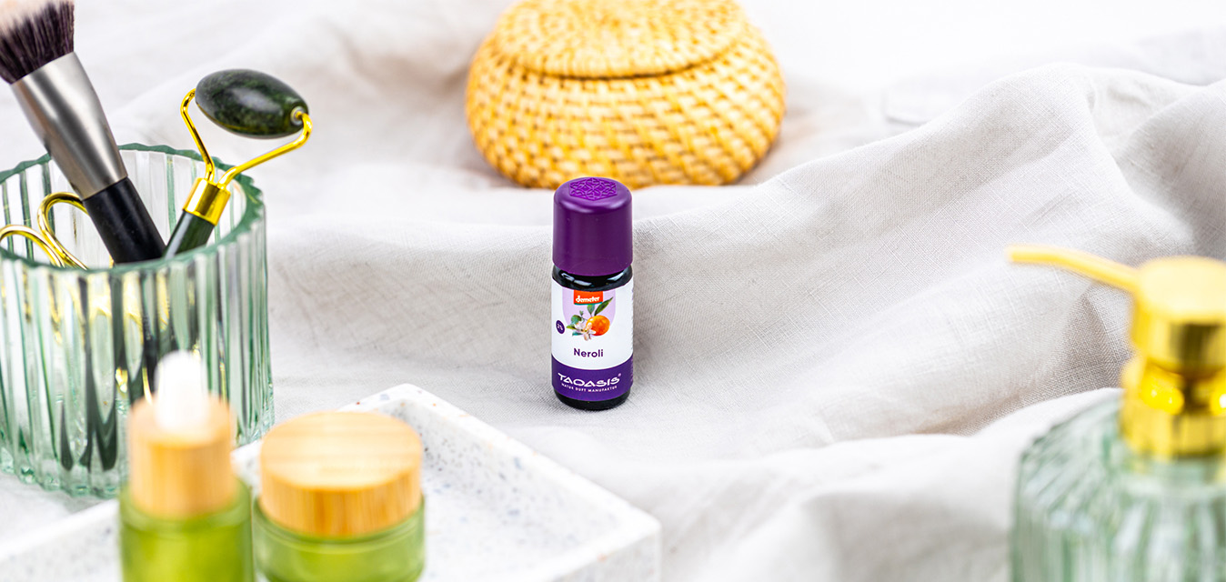 TAOASIS Neroliöl in einer hellen Wellness-Szene mit Gesichtsbürste, Jade-Roller, Pflegeprodukten und natürlichen Materialien.