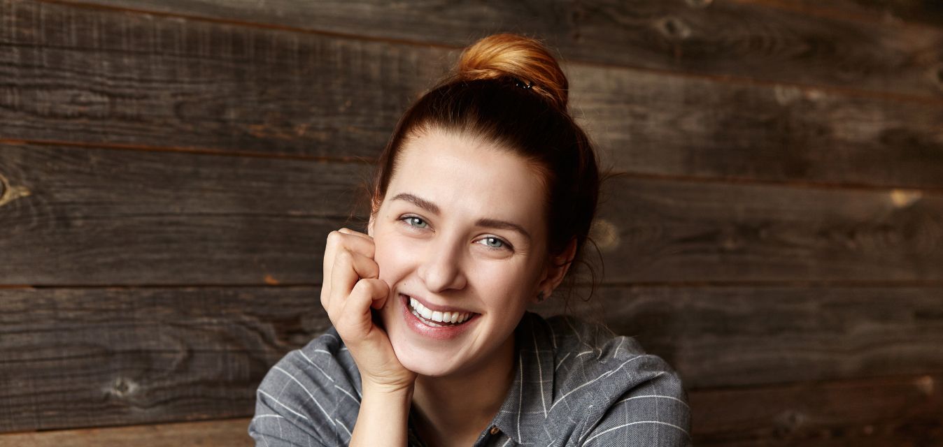 Lachende Frau mit Dutt, die sich auf Tisch abstützt.