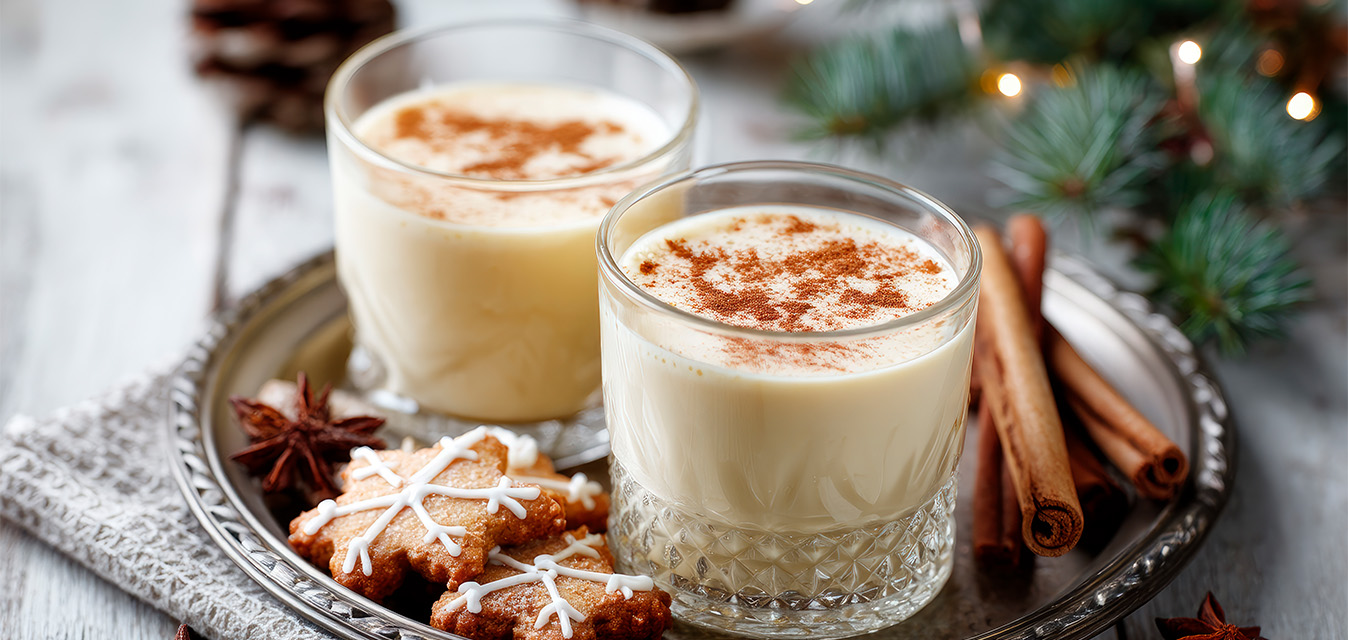 Zwei Gläser heiße Vanillemilch mit Zimt, dekoriert mit Zimtstangen, Sternanis und weihnachtlichen Keksen.
