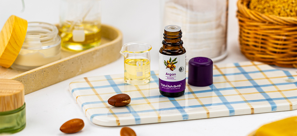 TAOASIS Argan Basisöl mit Arganfrüchten und kleinem Messbecher in einer hellen Pflegeszene mit natürlichen Accessoires.