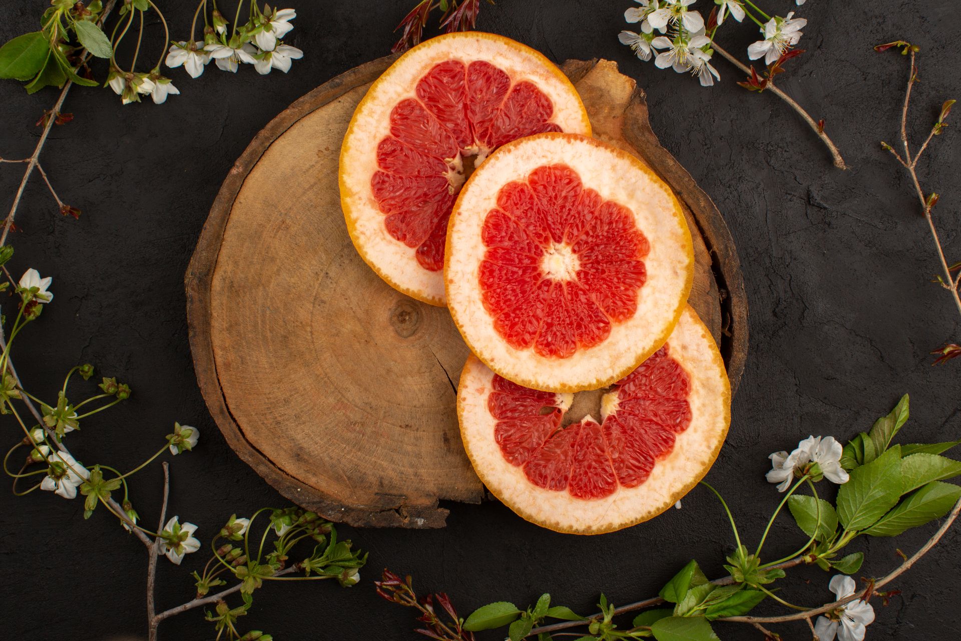 Aufgeschnittene Grapefruit auf Holzscheibe mit Blütenzweigen.