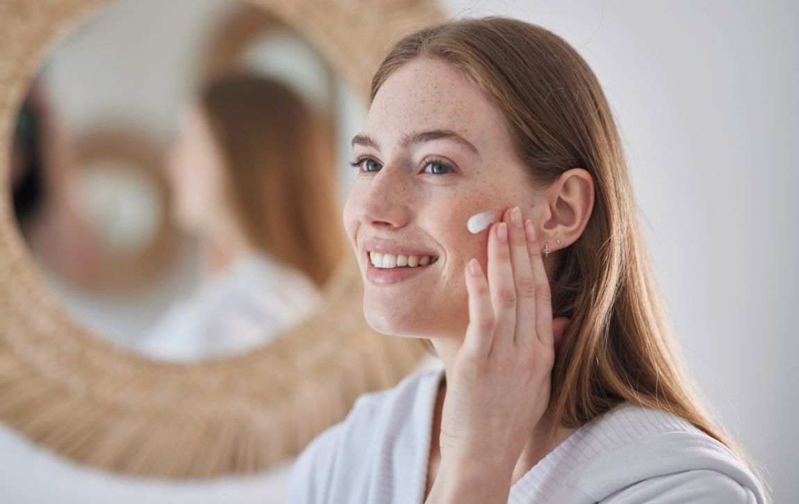 Model cremt sich das Gesicht vor Spiegel ein.