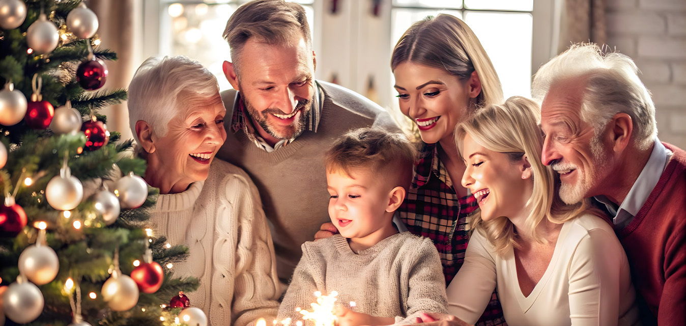 Mehrere Generationen einer Familie feiern gemeinsam Weihnachten neben einem festlich geschmückten Weihnachtsbaum.