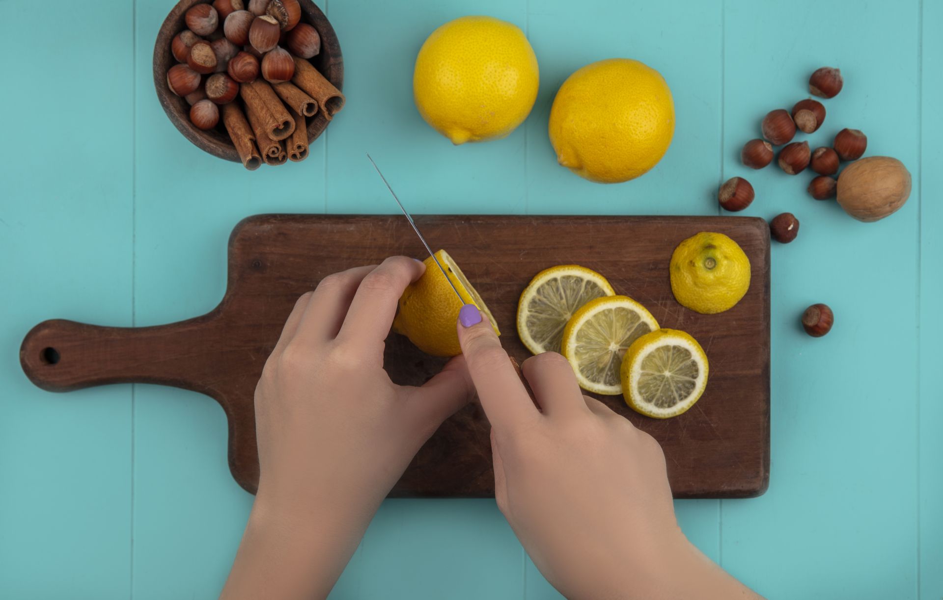 Hände schneiden Zitrone auf Holzbrett, daneben Zimt und Nüsse.