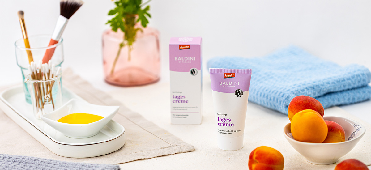 Baldini reichhaltige Tagescreme in einer hellen Pflegeszene mit Aprikosen, Handtuch und natürlichen Beauty-Accessoires.
